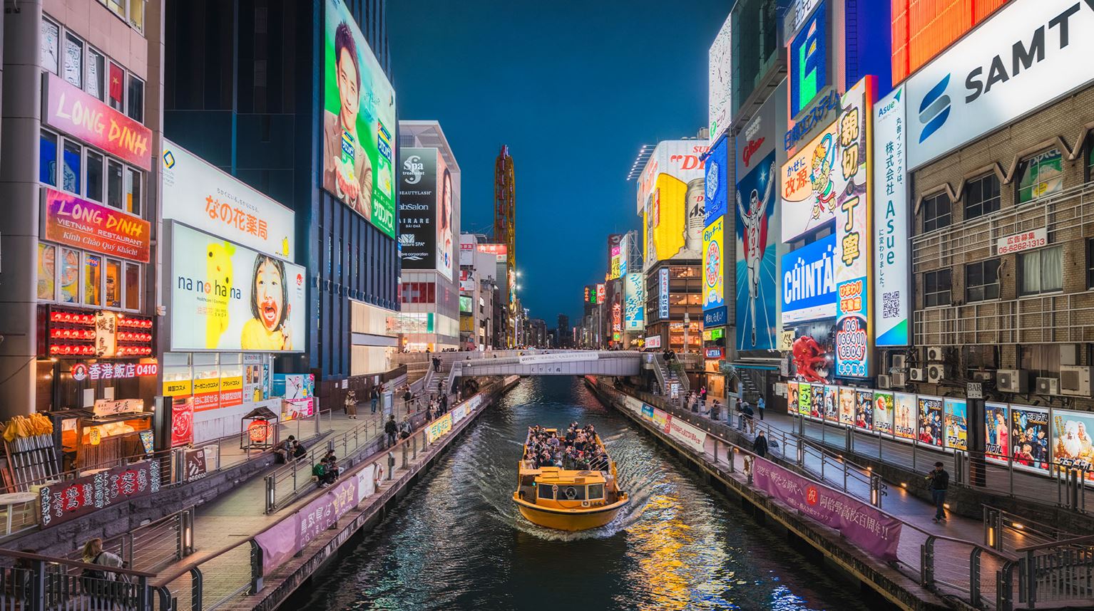 Bright neon signs surrounding a canal at night