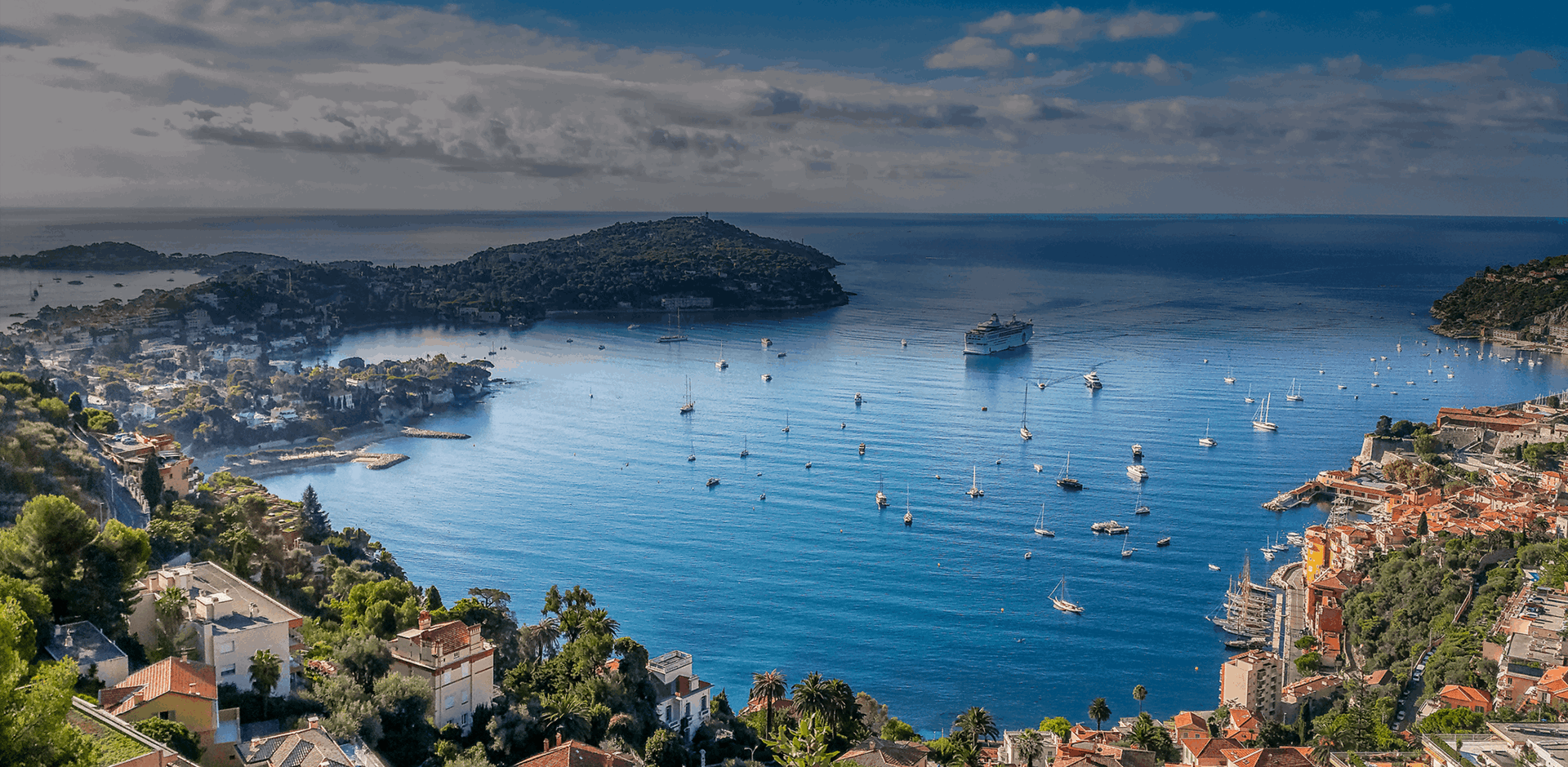 View from the top of the town overlooking houses and small boats with a cruise ship in the Bay Of Villefranche-Sur-Mer, France