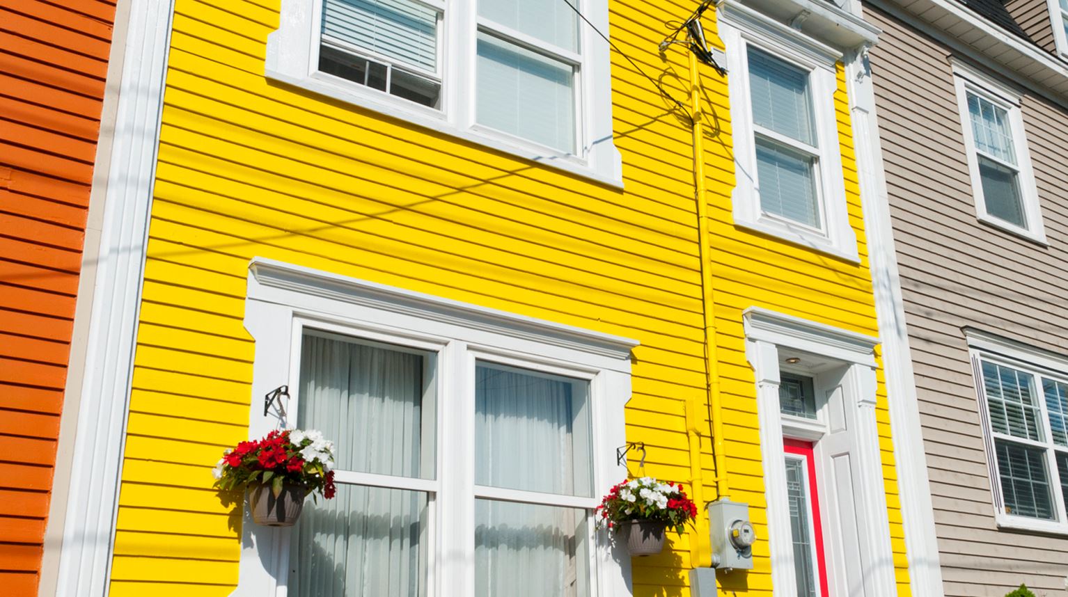 Bright yellow house with red outside wooden chairs in front of the window with flowers, St John's Colourful Clapboard, Newfoundland, Canada