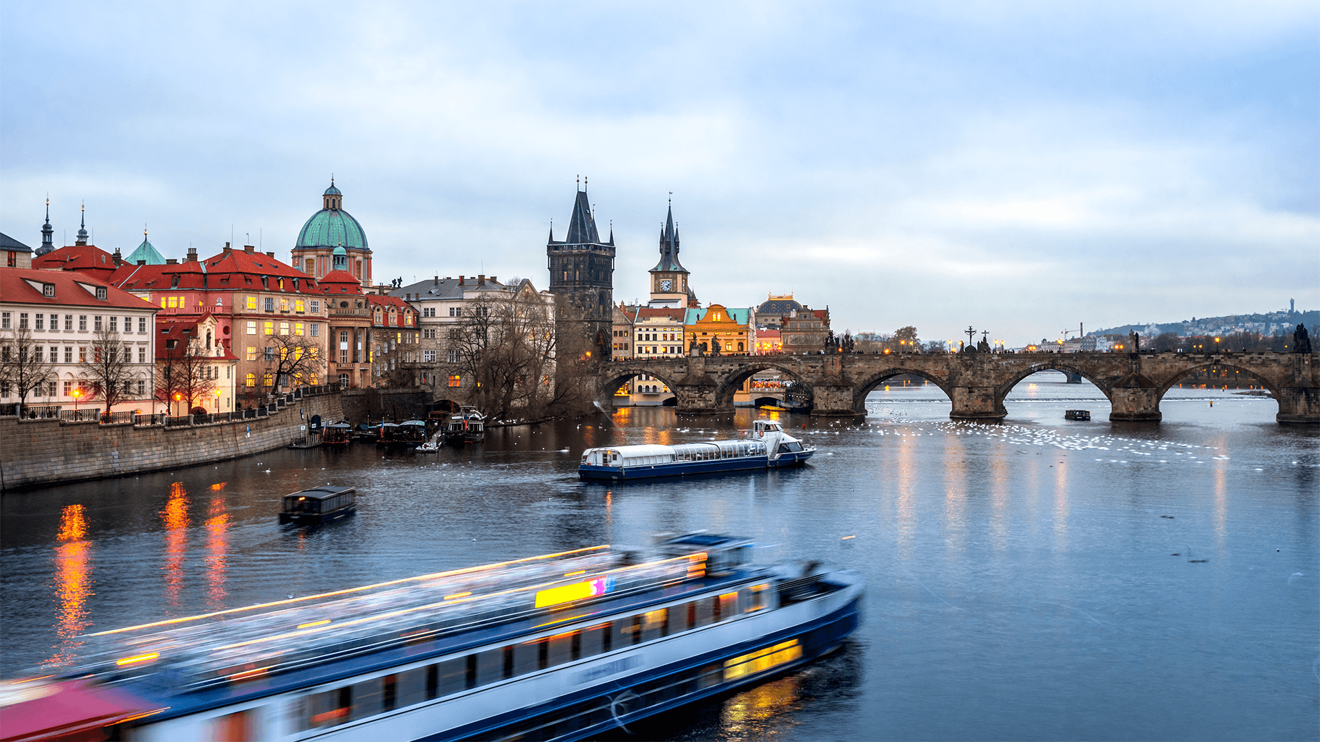 Tour boat gliding towards the Charles Bridge at dusk