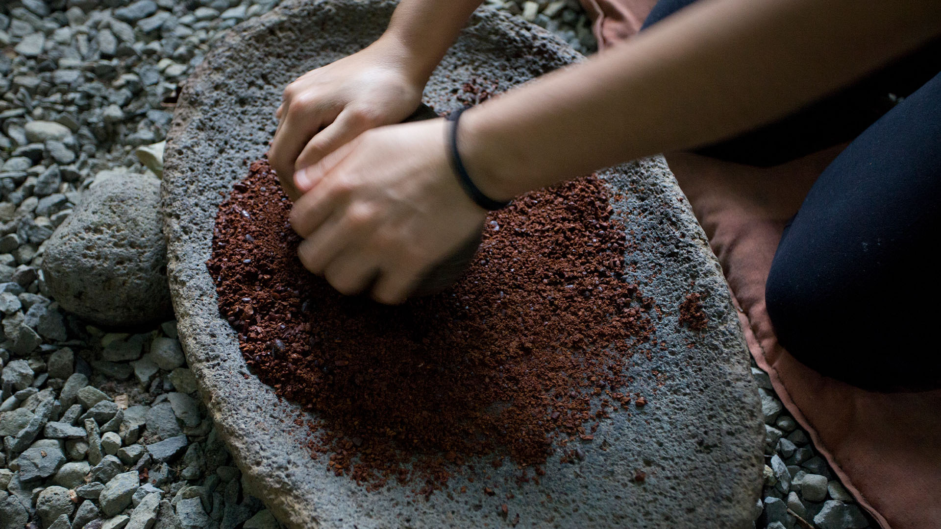 Hands manually grinding cocoa beans in a stone bowl