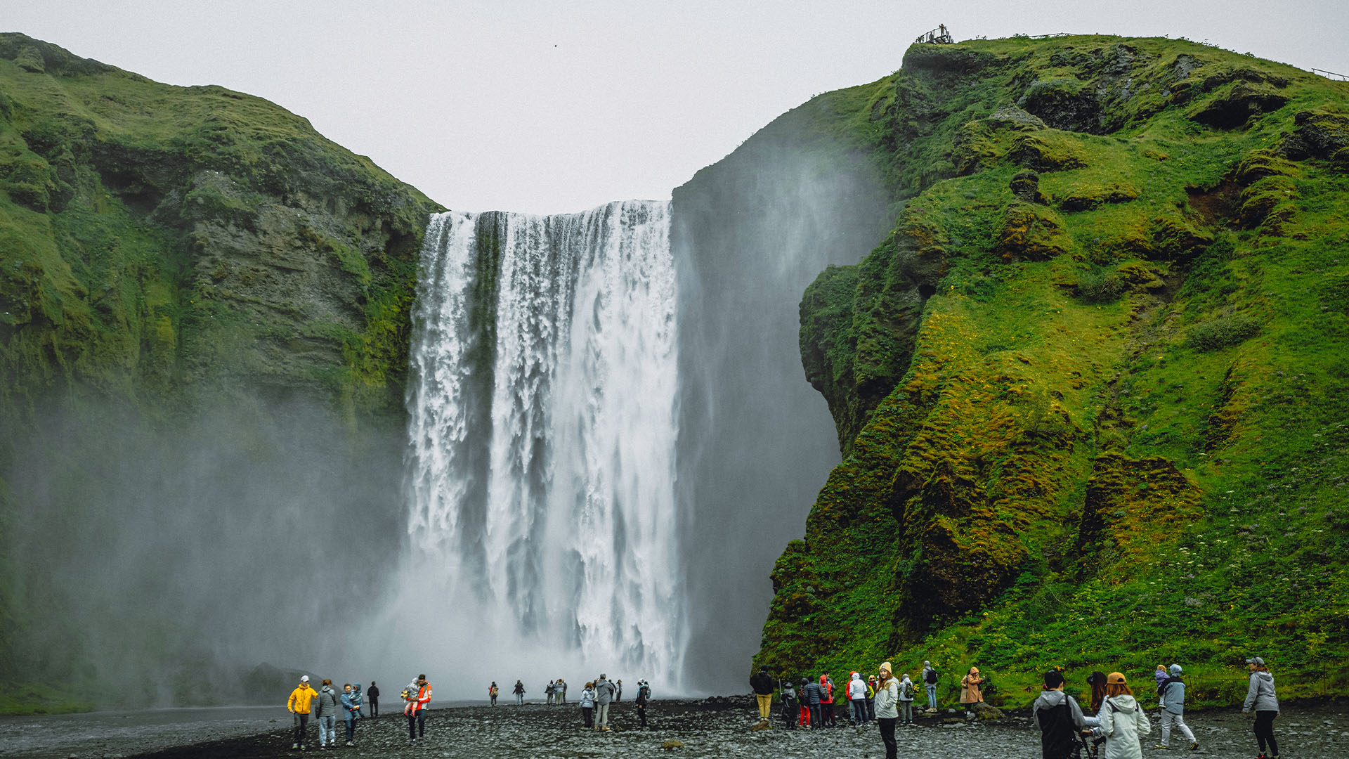 Visitors standing at the base of Skógafoss waterfall