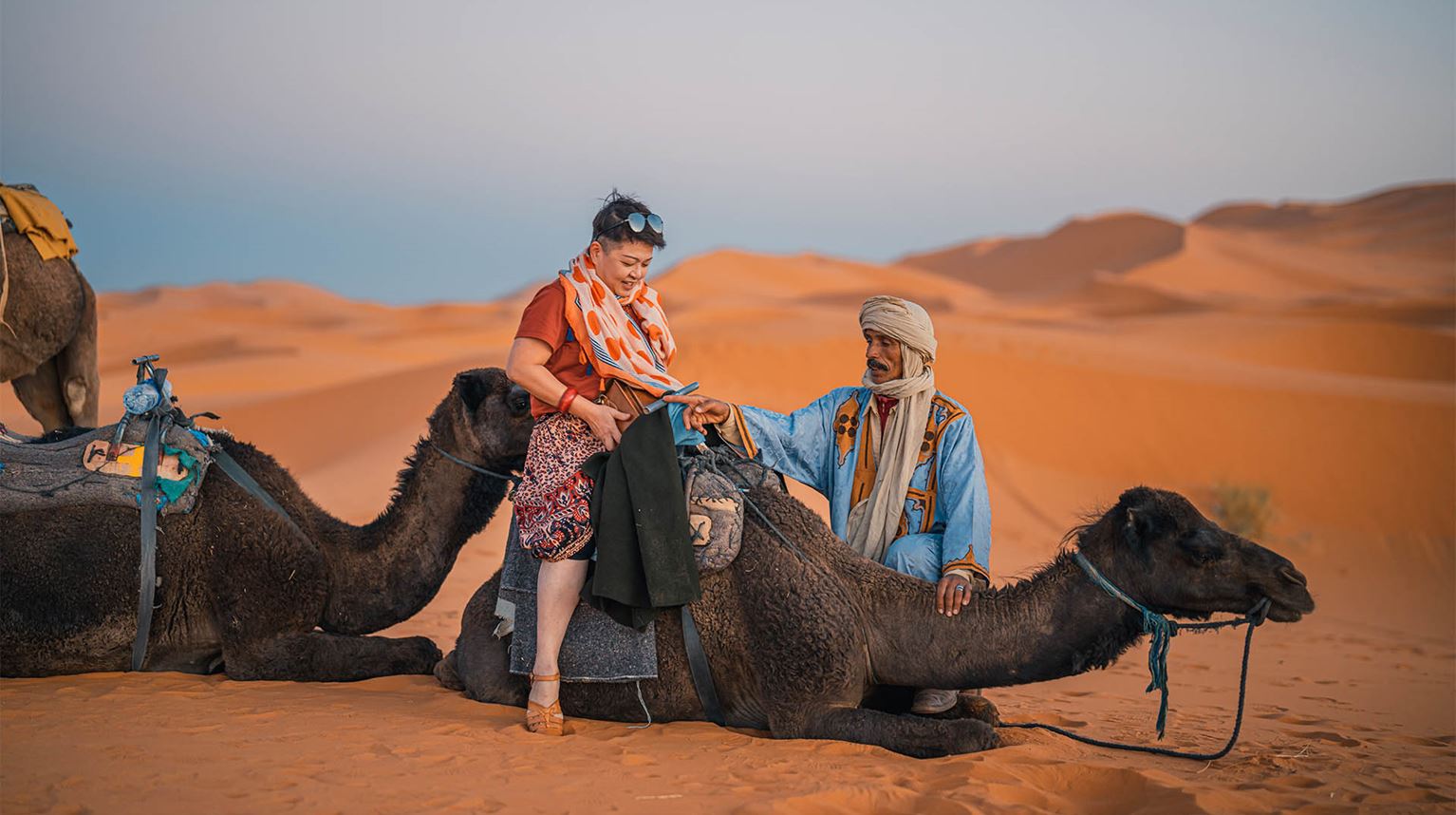Woman riding on camel that is just about to rise from desert