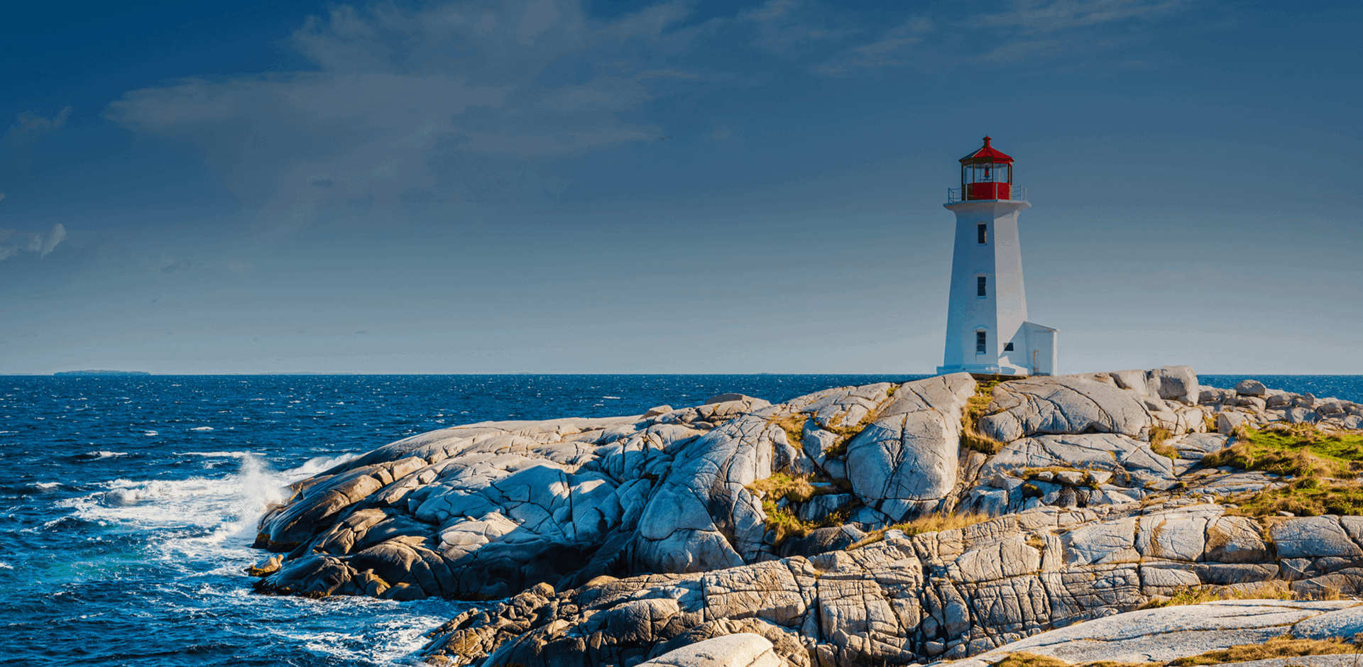View of Peggy's Cove Lighthouse over rocky hill by the ocean under Summer Sky, Nova Scotia, Canada.