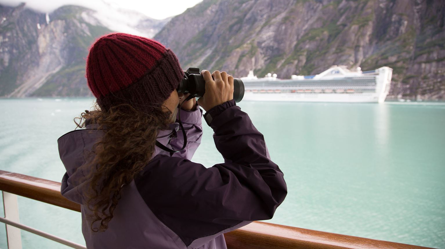 Woman on a ship overlooking the ocean using binoculars 