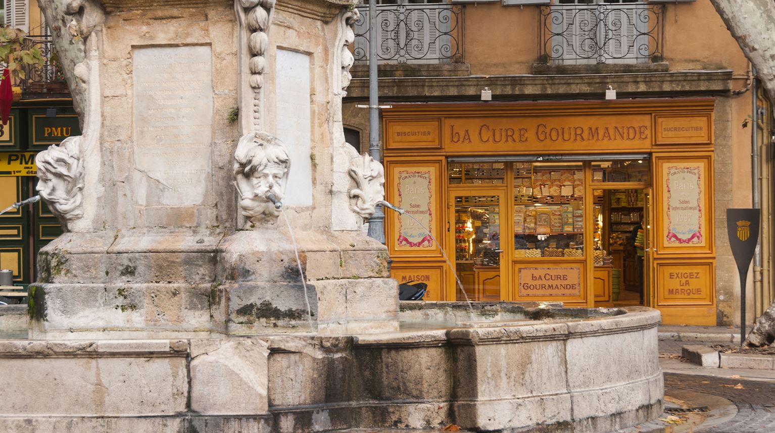 Ornate stone fountain outside a gourmet shop. 