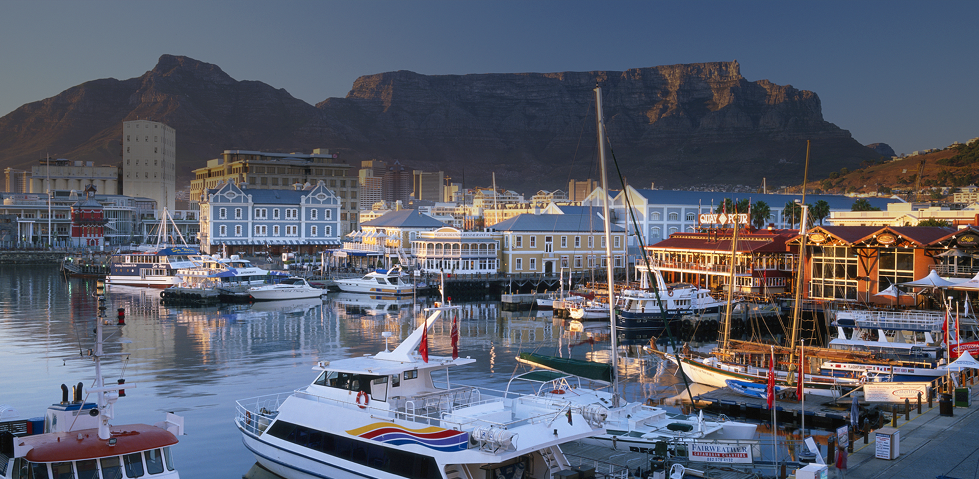 Waterfront town with boats in harbor with Table Mountain in background, South Africa.