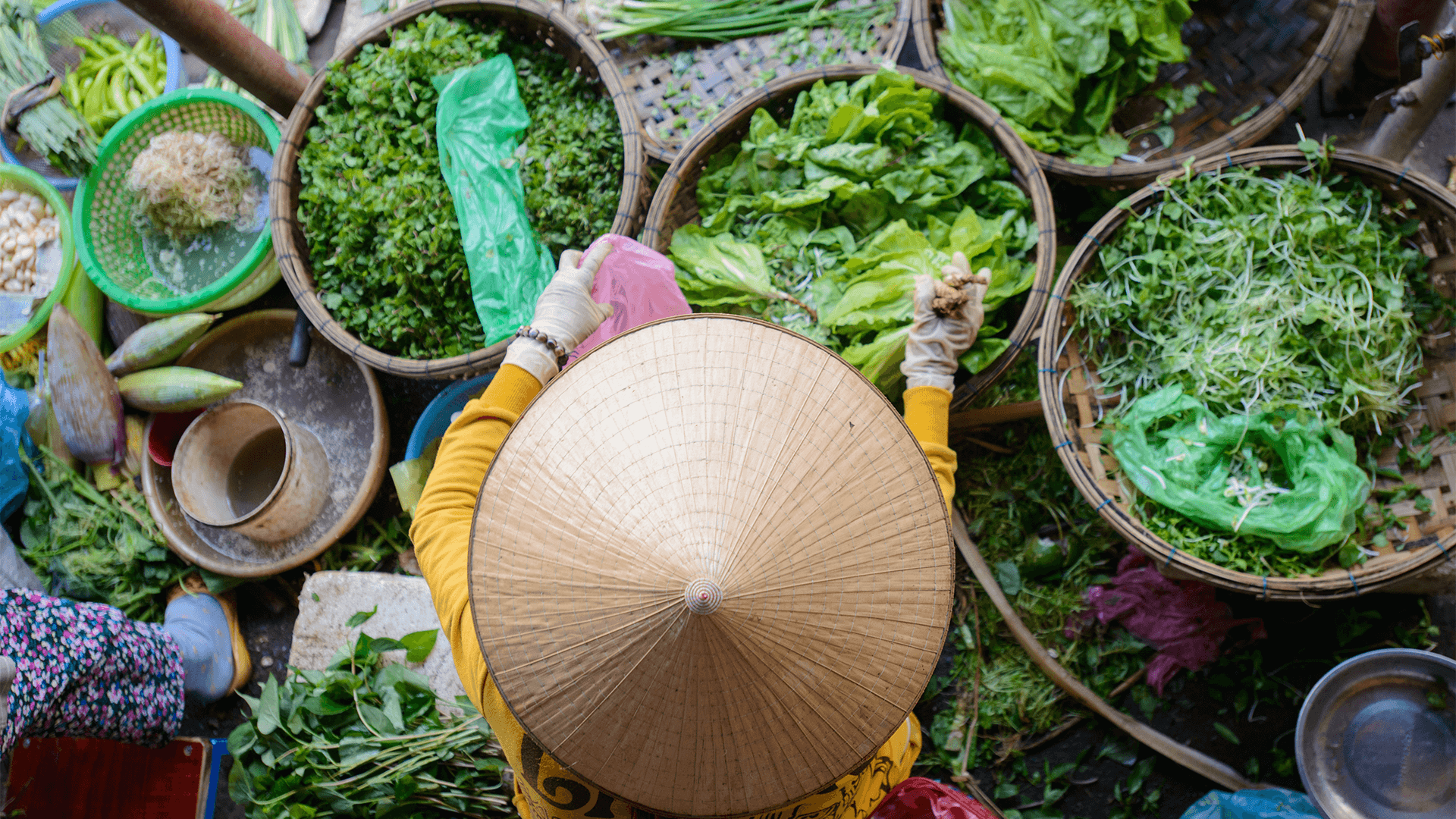 Vendor in conical hat selling fresh greens at market 