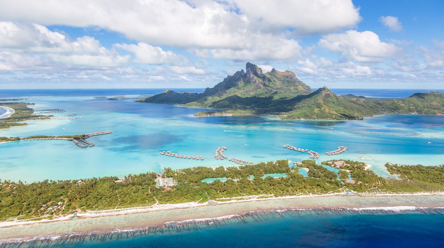 Aerial view of a turquoise lagoon with Bora Bora volcano in the background.      
