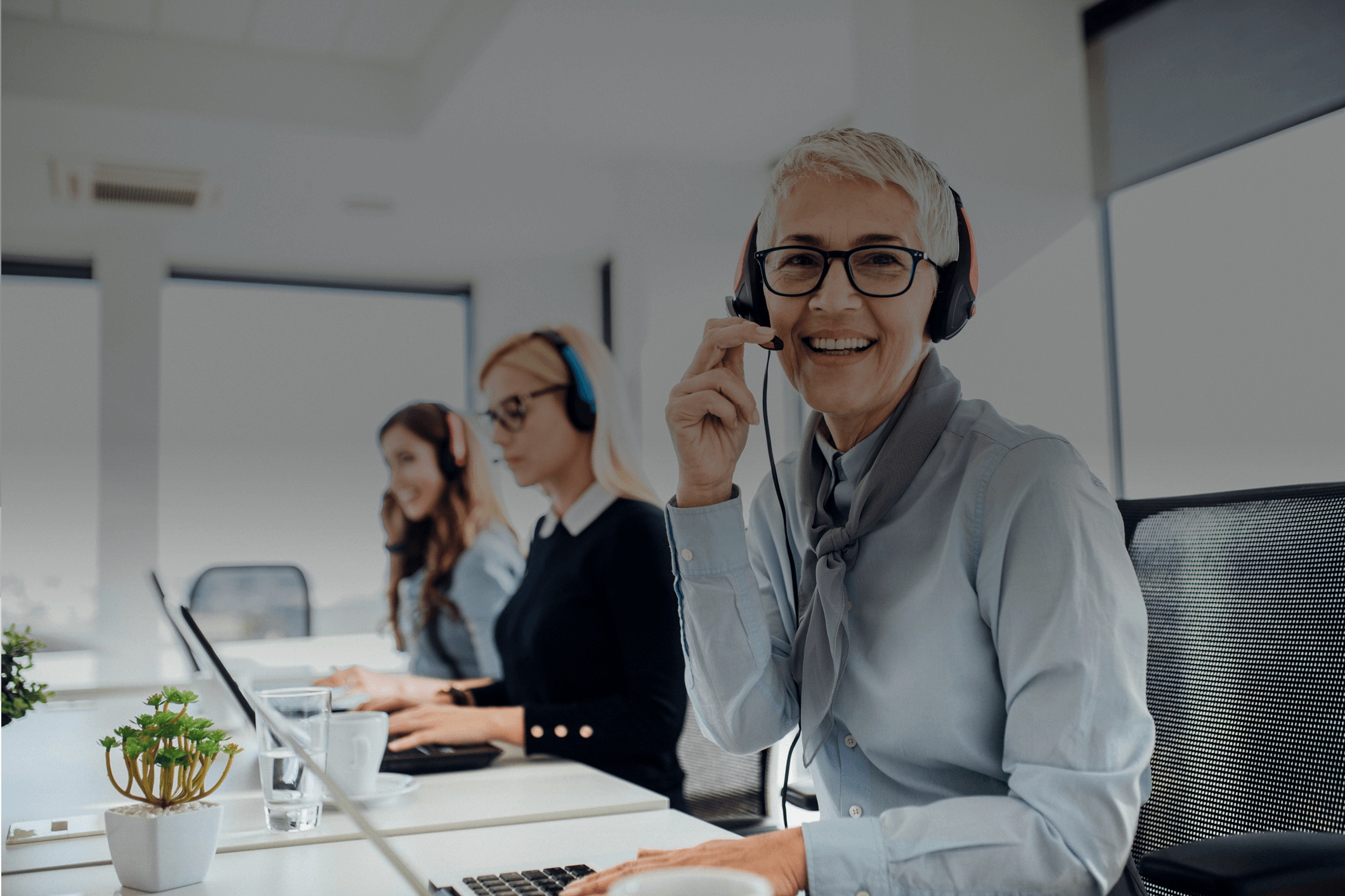 Joyful call center agent in the office with other agent taking a reservation booking over the headset. 
