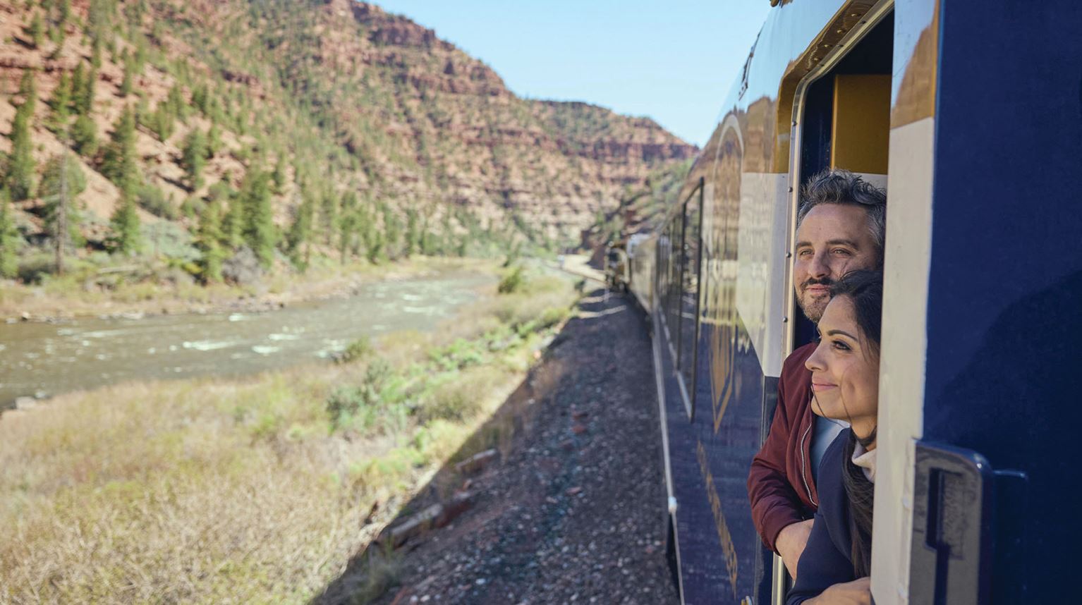 Two travellers looking the Red Canyon landscape on the outdoor viewing platform of a train