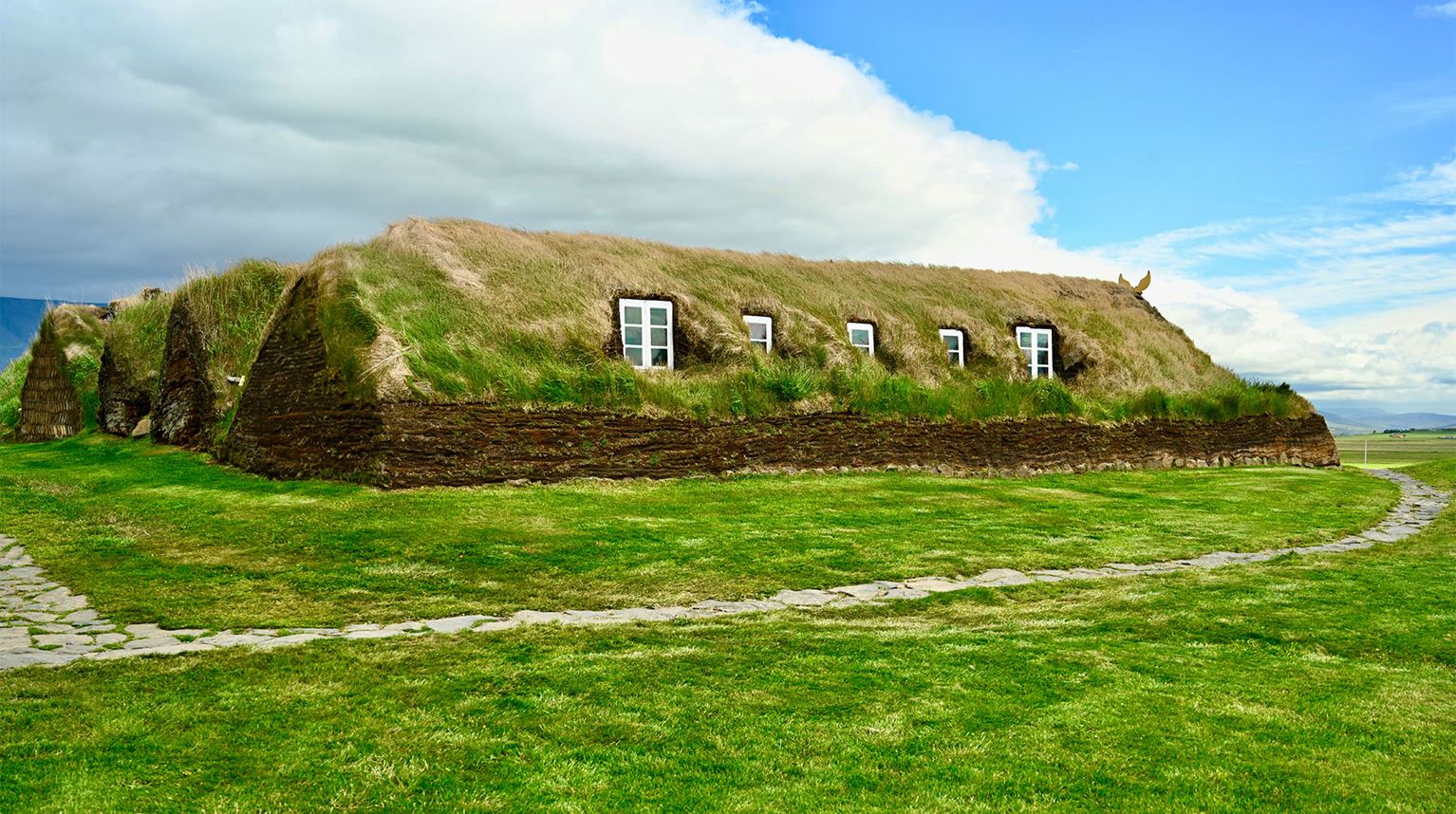 Exterior of a stone Viking Longhouse covered in grass.