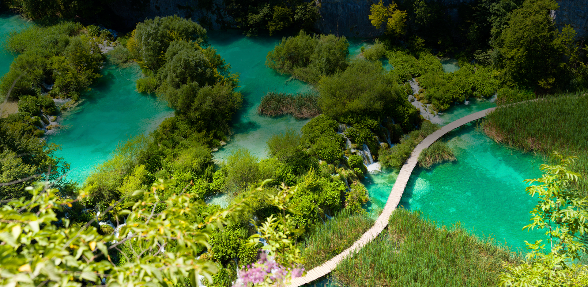 Two tourists walking on wooden bridge passing by waterfalls.