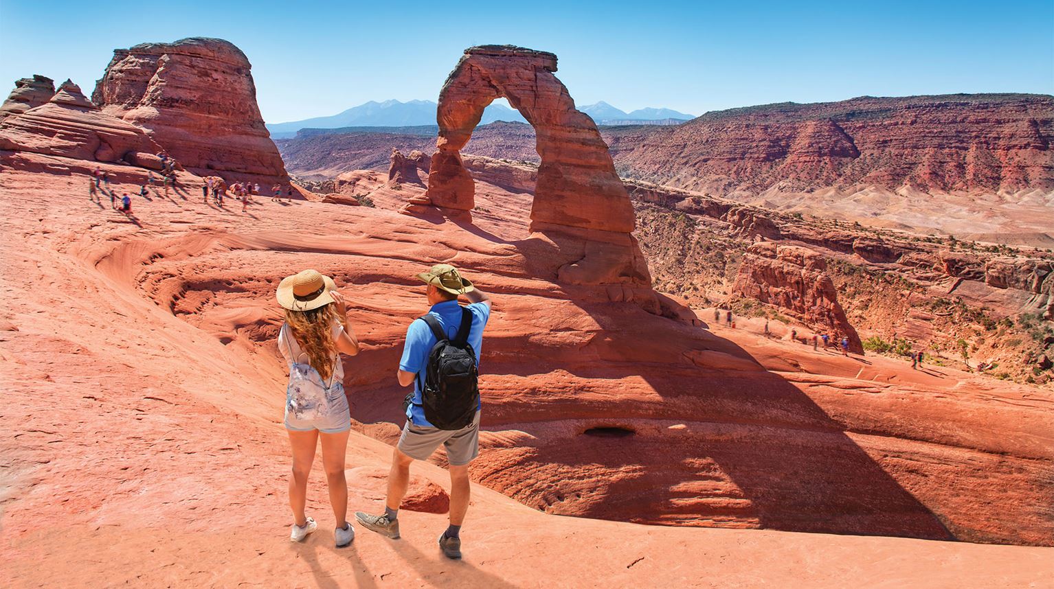Travellers hiking and looking at an natural arch structure in the Arches National Park, Utah 