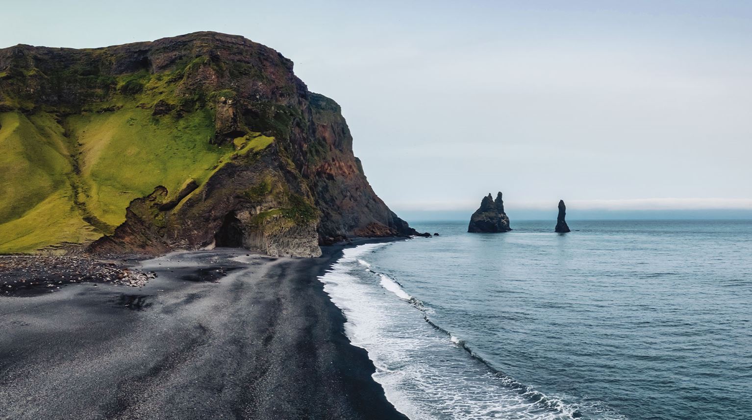 Beach made of black sand next to grass covered cliffs