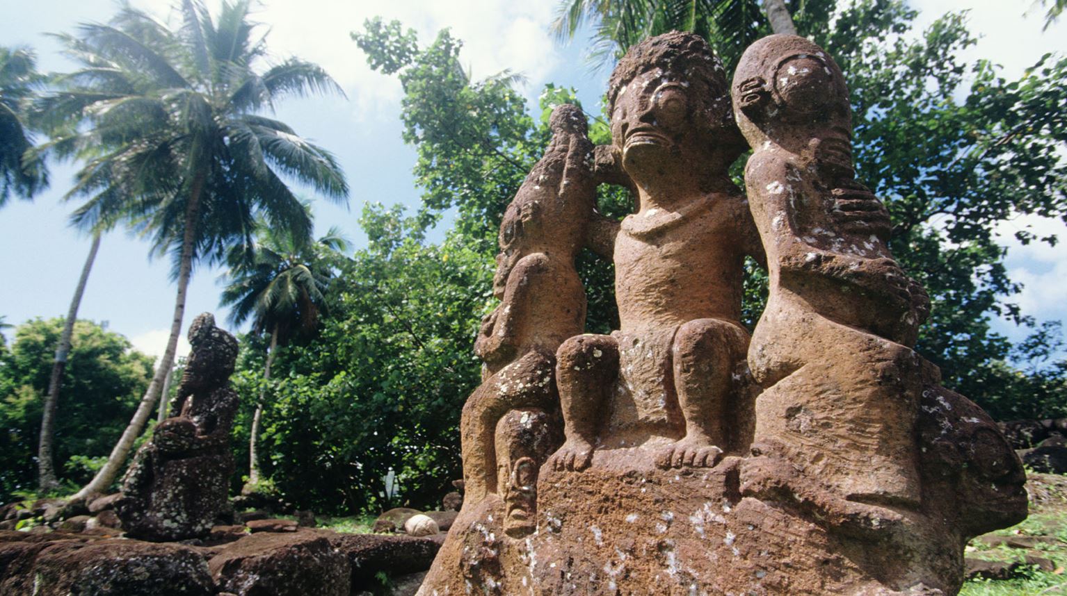 Trio of ancient carved stone tiki statues in a jungle clearing